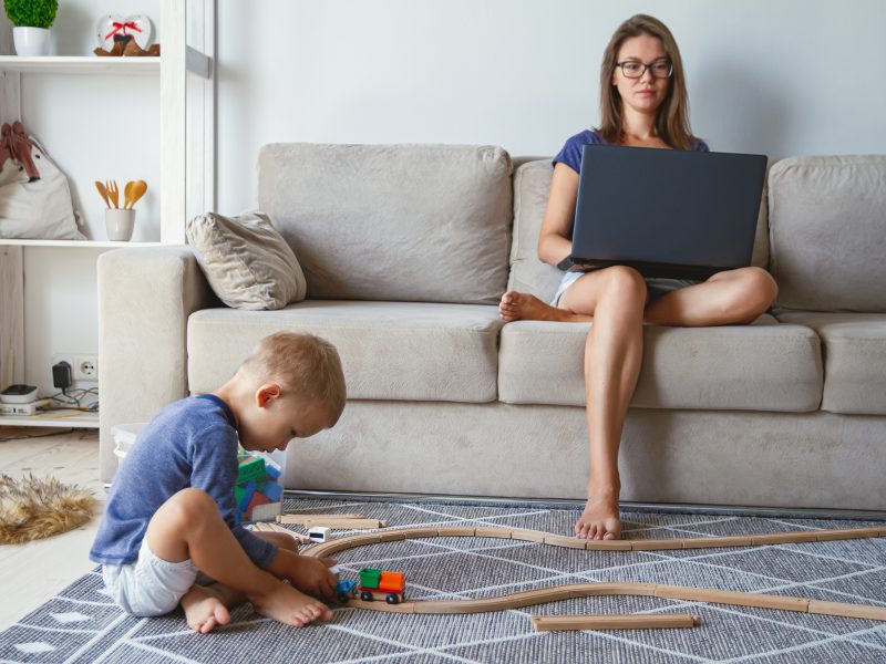 Donna Al Lavoro Sul Divano Con Bambino Che Gioca