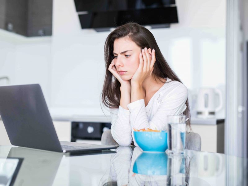 Attractive Young Woman Using Laptop At Breakfast And Sitting In The Kitchen